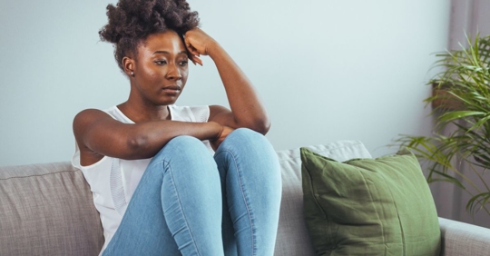African American woman sitting on couch and feeling depressed